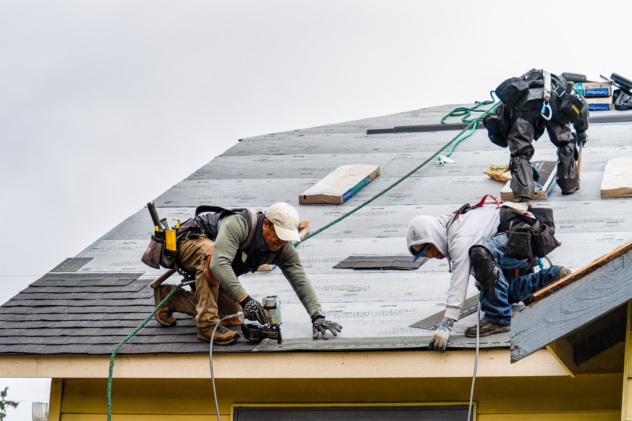 Crew Installing New Shingles on Roof on a Rainy Day